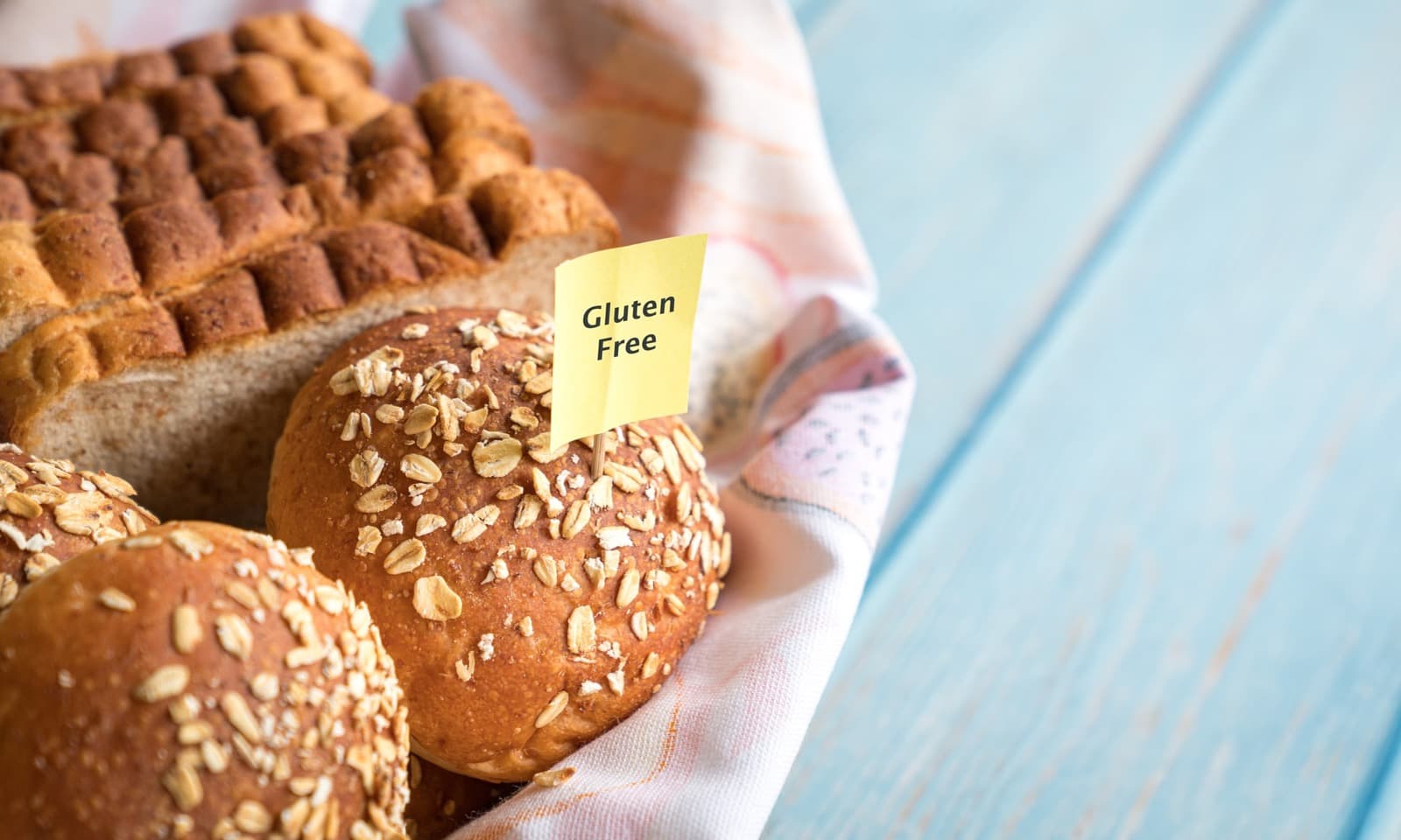 Cesta con panes y bollos rotulados «sin gluten» sobre un paño de cocina