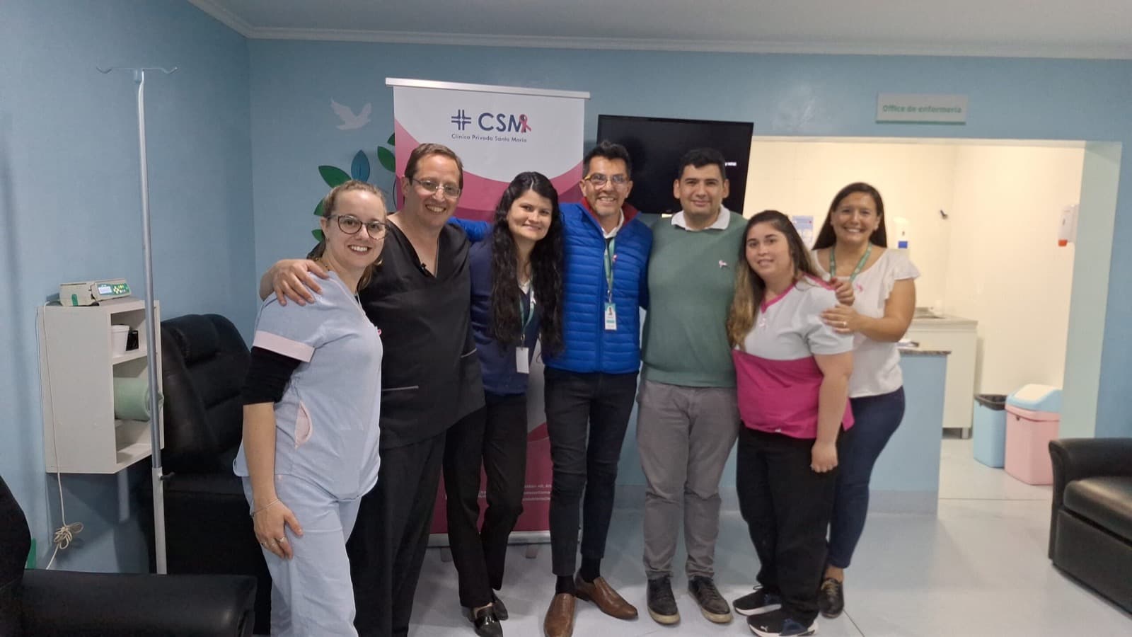 Equipo de la Clínica Privada Santa María reunido en el Hospital de Día frente al banner institucional de Octubre Rosa