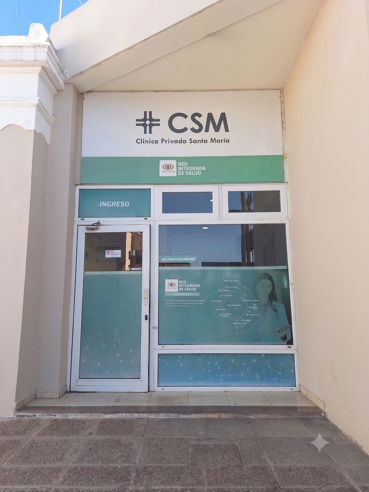 Ingreso al Hospital de Día de la Clínica Privada Santa María en Belisario Roldán 89: puerta de vidrio con el logo CSM sobre el dintel y la vidriera de la Red Integrada de Salud del Hospital Italiano